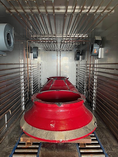 Two red cone crusher mantles loaded on the roller bed inside a DCI chamber